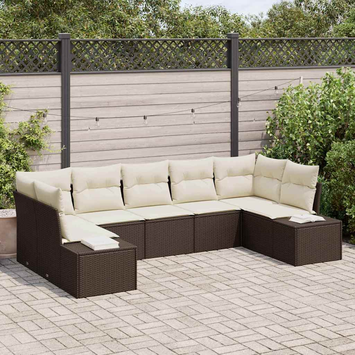 Outdoor-Ecksofa mit cremefarbenen Kissen auf einer Backstein-Terrasse. Im Hintergrund ist ein Holzzaun mit Pflanzen.