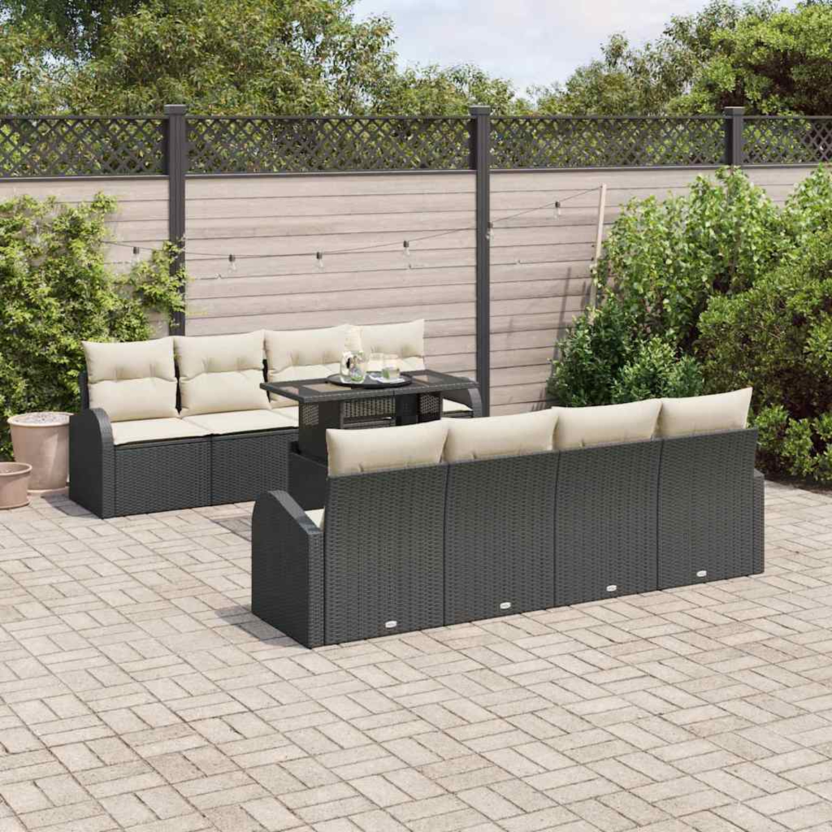 Garten-Terrassen-Set. Dunkelgraue Korbsessel mit beigen Kissen, ein kleiner Tisch und ein Holzzaun im Hintergrund. Gepflasterter Boden.