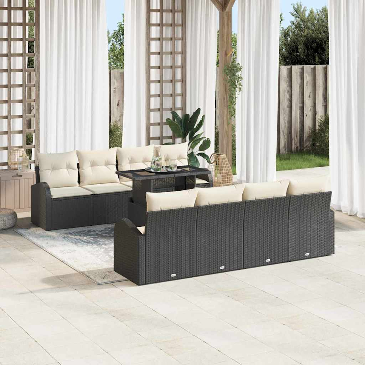 Terrassenset mit schwarzen Korbsesseln, beigen Kissen und einem Tisch mit Glasplatte, vor weißen Vorhängen und einem Holzgitter.