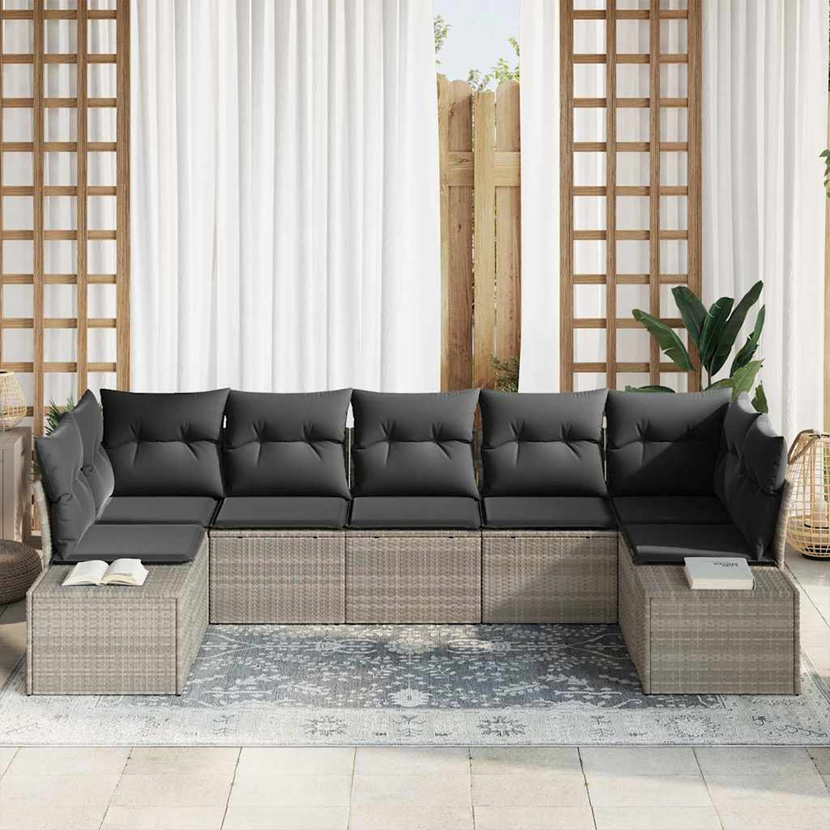 Un sofá seccional gris para exteriores con cojines oscuros sobre una alfombra. Cortinas blancas y enrejado de madera detrás.