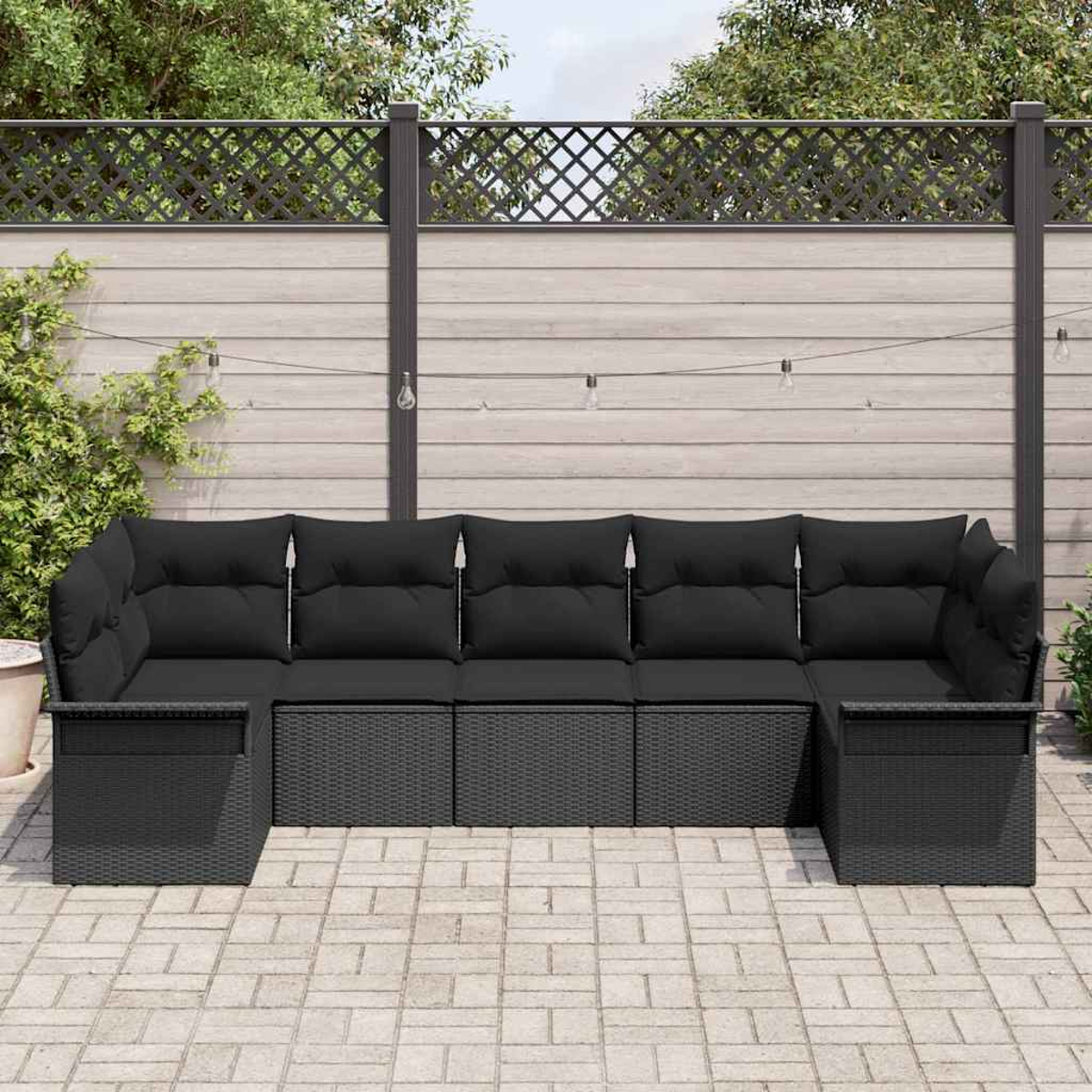 Ein schwarzes Outdoor-Sofa aus Korbgeflecht mit Kissen. Es steht auf einer Ziegelterrasse, mit einem Zaun und Grün im Hintergrund.