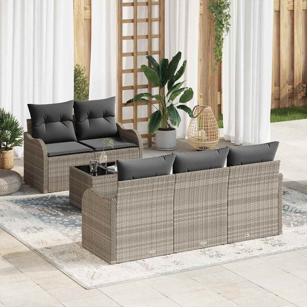 Gartenmöbel-Set mit grauen Kissen. Enthält ein Zweisitzer, Sofa und Couchtisch. Pflanzen und Vorhänge im Hintergrund.
