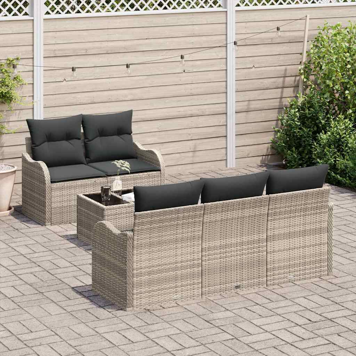 Gartenmöbel-Set: Zweisitzer, Dreisitzer-Sofa und Couchtisch. Dunkelgraue Kissen, hellbraunes Korbgeflecht und Holzzaun.