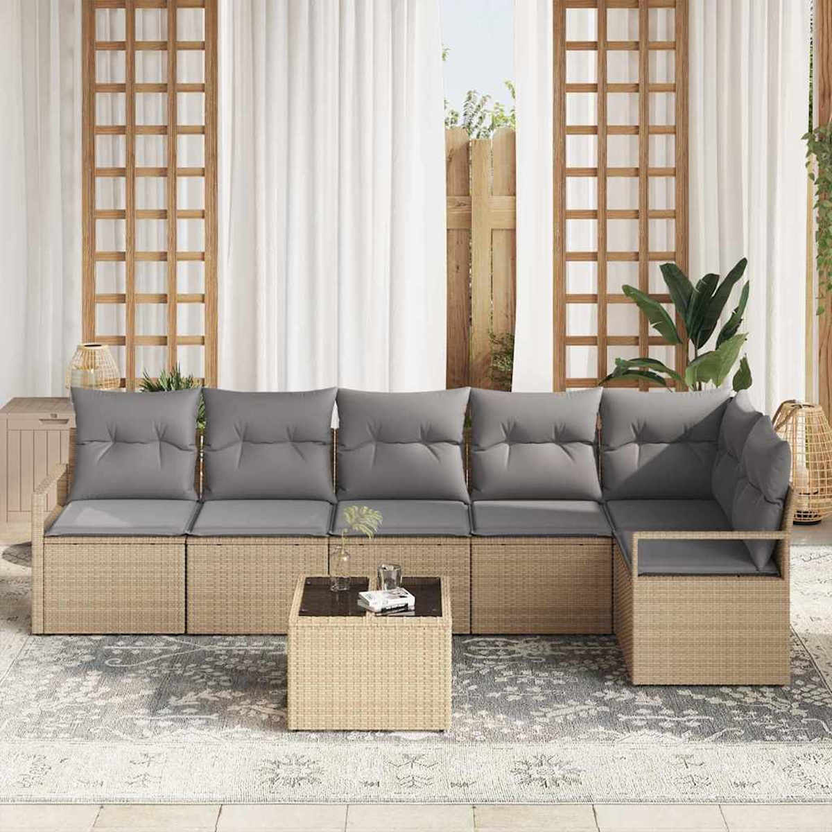 Ein Ecksofa im Freien mit grauen Kissen und einem passenden Couchtisch steht auf einem gemusterten Teppich. Weiße Vorhänge und ein Fenster sind im Hintergrund.
