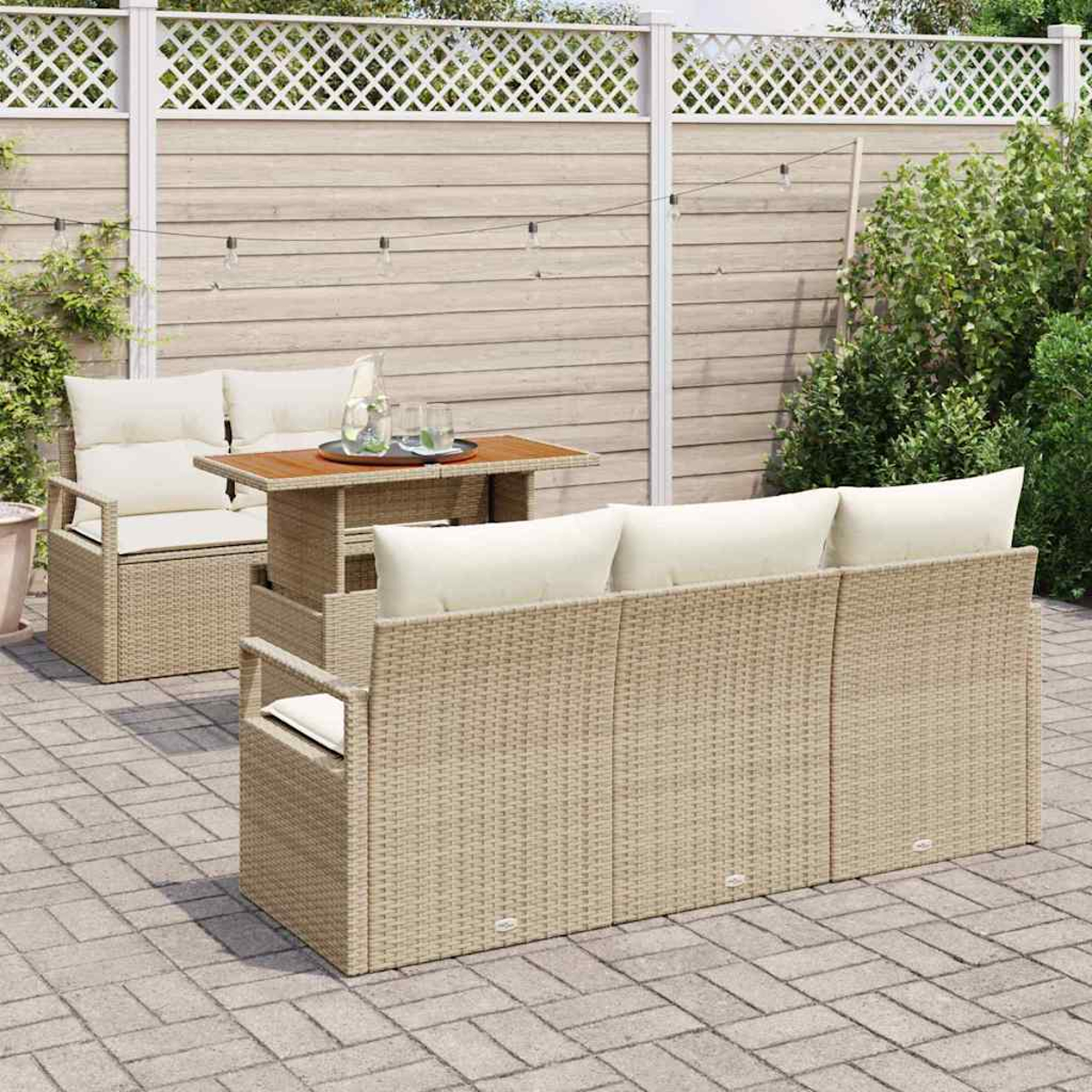 Terrassenset im Freien mit Korbmöbeln, Tisch und Kissen. Dahinter ein hellbrauner Holzzaun und üppiges Grün.