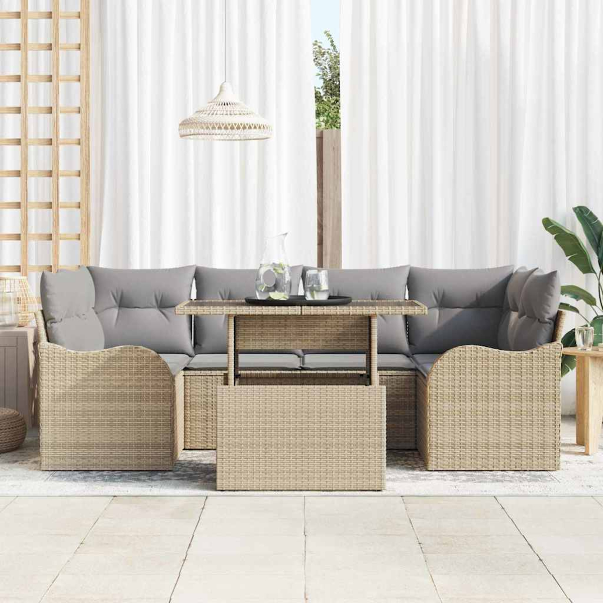 Juego de muebles de mimbre para exteriores con cojines grises. Mesa con vidrio y jarra de agua. Cortinas blancas y lámpara colgante.