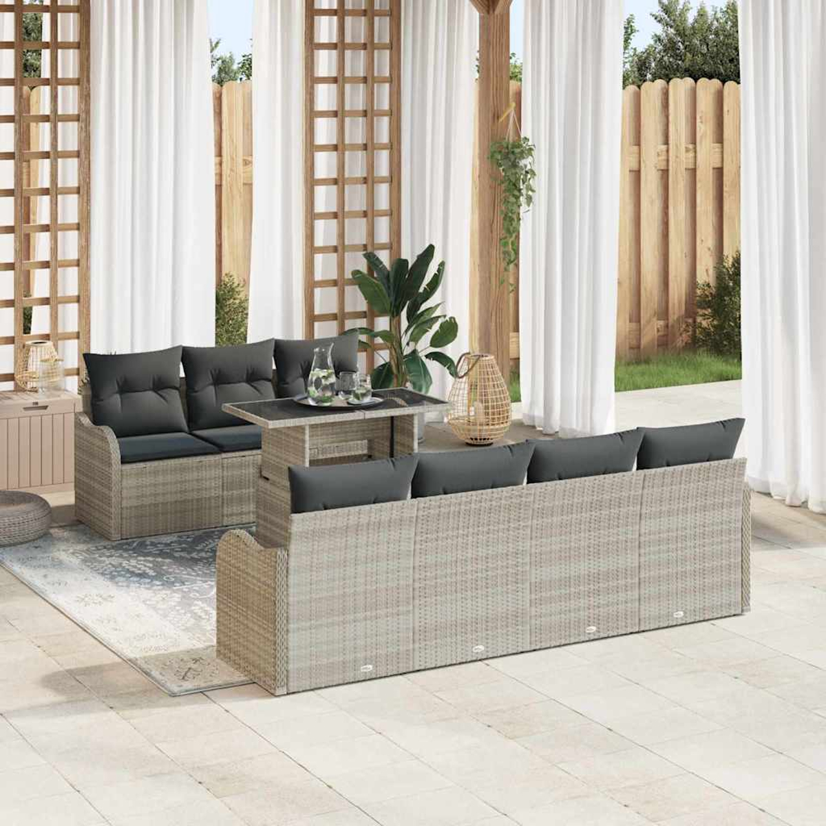 Terrassengarnitur mit grauen Kissen, Tisch und Dekorationsartikeln. Weiße Vorhänge und Holzzaun im Hintergrund.