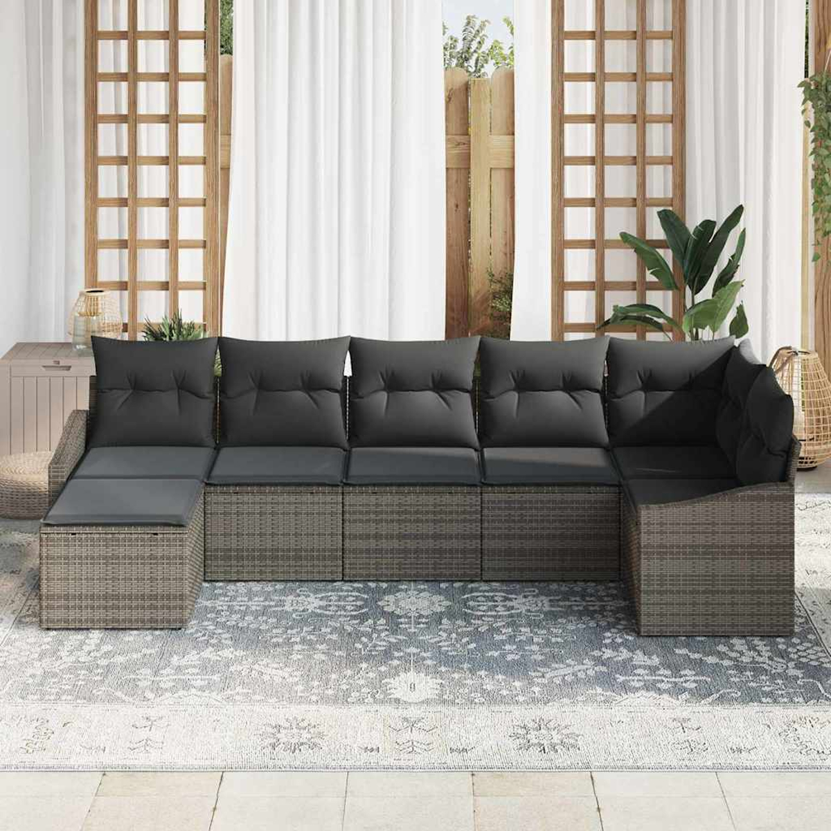 Outdoor-Ecksofa mit grauen Kissen. Beiger Korbboden, grauer Teppich, weiße Vorhänge. Pflanzen und Holzgitter im Hintergrund.