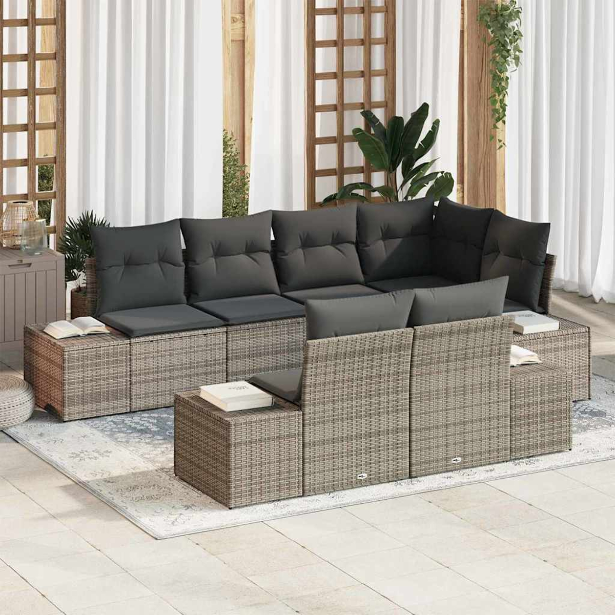 Sofá seccional exterior con cojines grises, libros y alfombra. Enrejado de madera y cortinas blancas al fondo. Se ven plantas.