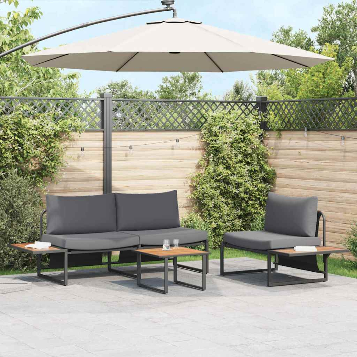 Gartenmöbel-Set mit grauem Sofa, Stuhl und Tisch unter einem beigen Sonnenschirm. Holzzaun und Grün in Hintergrund.
