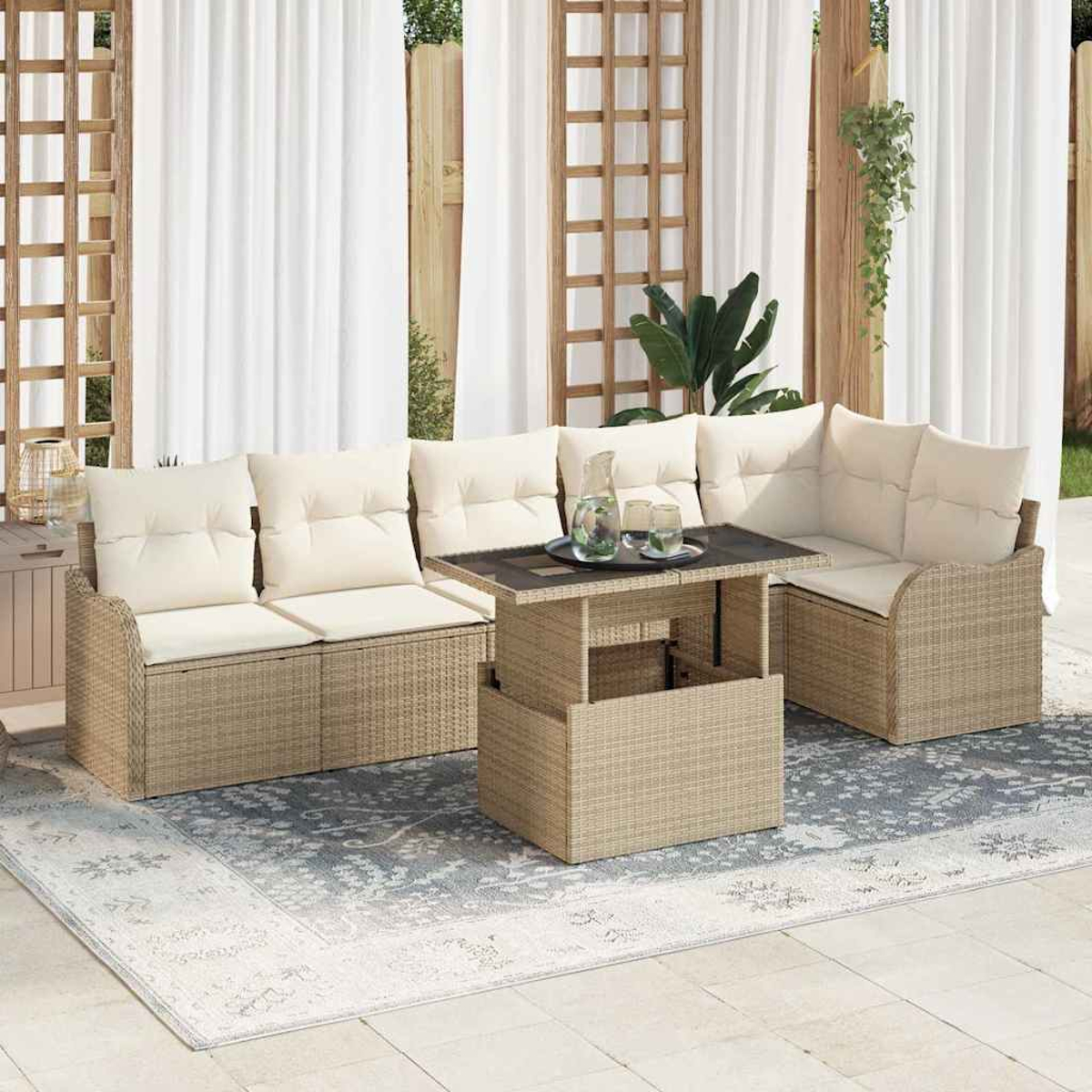 Gartenmöbel-Set aus Korbgeflecht mit beigefarbenen Kissen und einem Tisch mit Hubfunktion auf einem gemusterten Teppich. Weiße Vorhänge im Hintergrund.