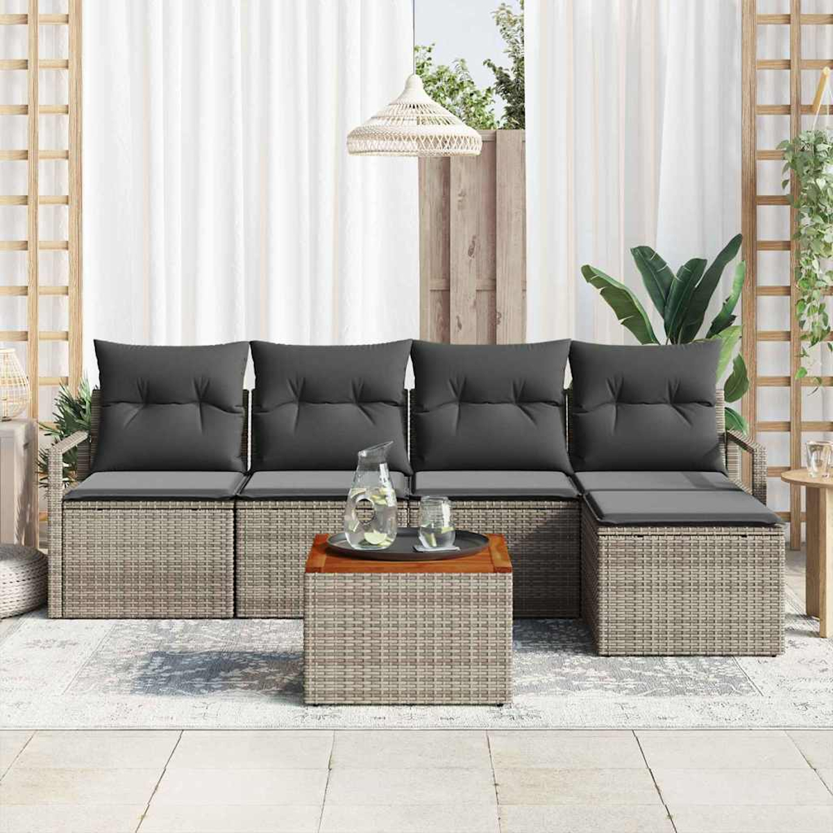 Terrassenset im Freien mit grauen Kissen und einem Holztisch mit Getränken. Weiße Vorhänge und Pflanzen im Hintergrund.