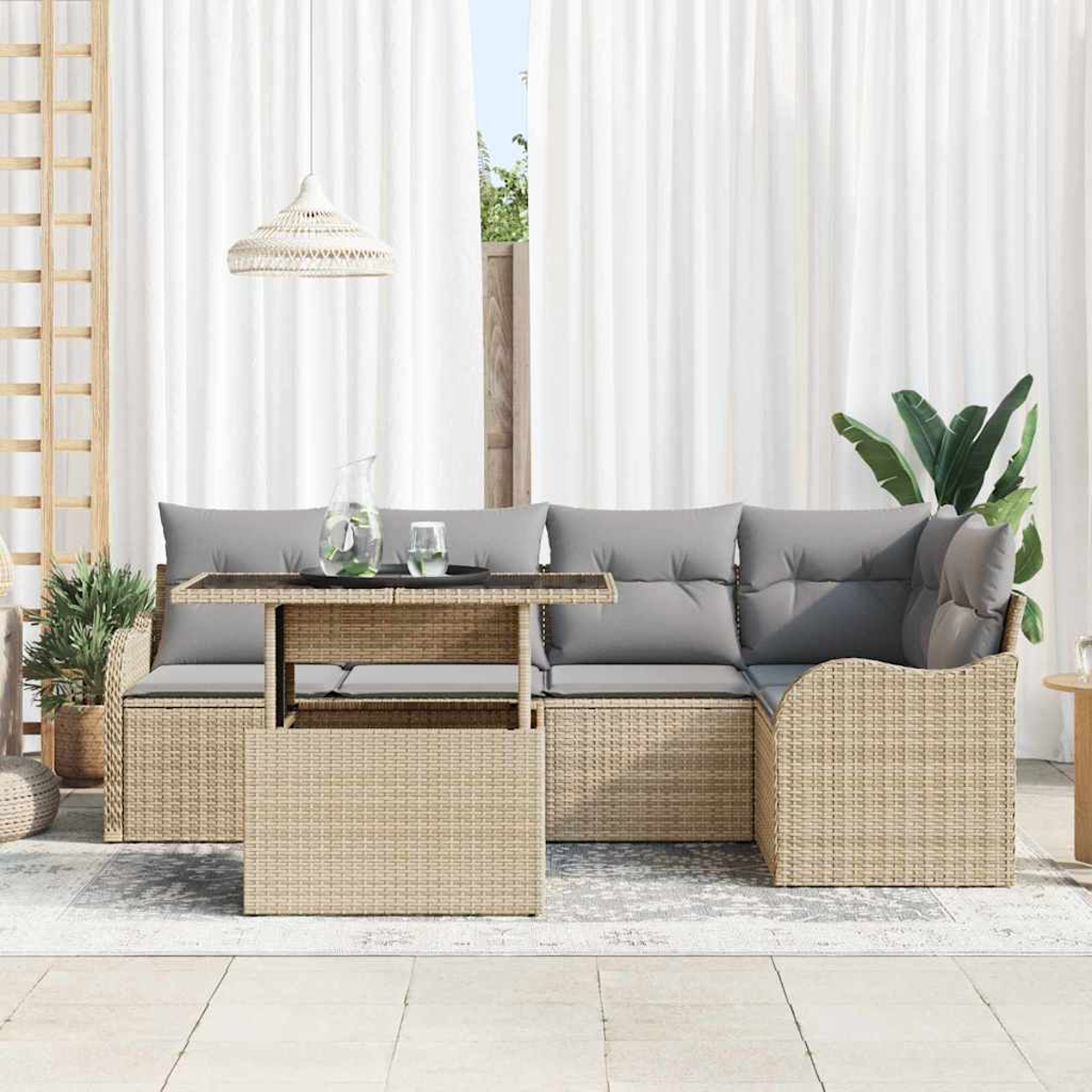 Gartenmöbel-Set aus Korbgeflecht mit grauen Kissen, einem Tisch und einem weißen Vorhang im Hintergrund. Pflanzen und eine Hängelampe sind vorhanden.
