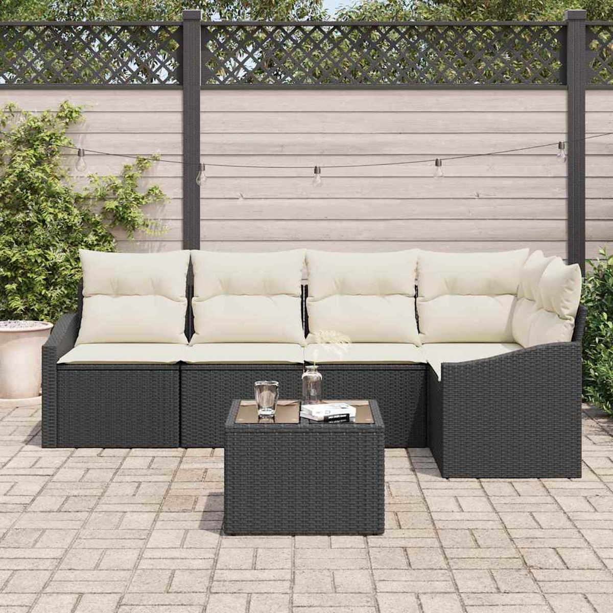 Outdoor-Ecksofa mit cremefarbenen Kissen und einem kleinen Tisch. Ein Holzzaun und Lichterketten im Hintergrund.