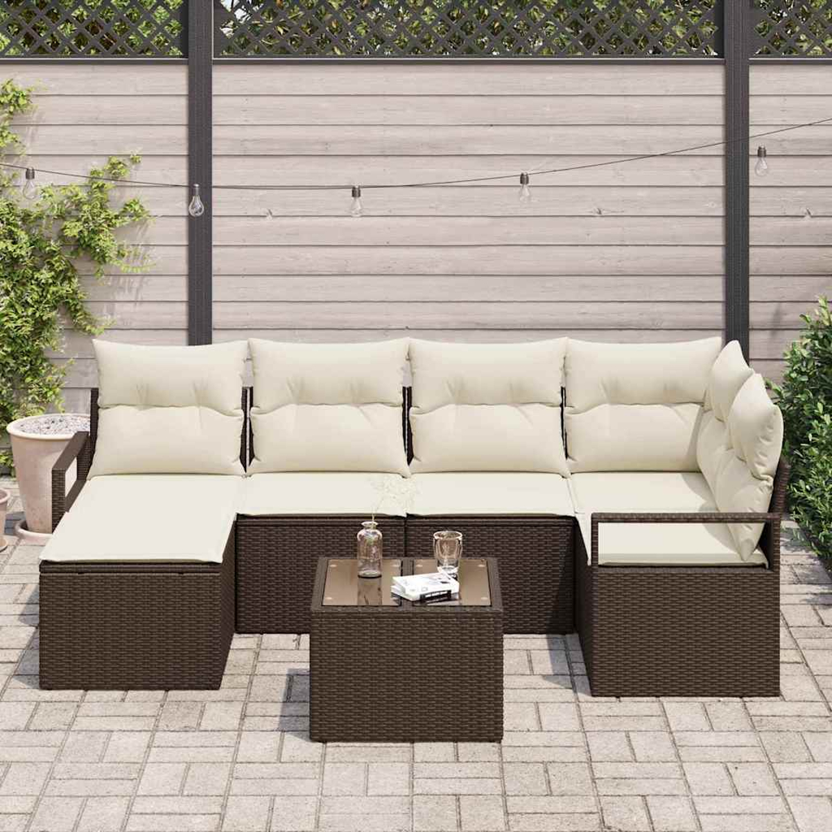 Gartenmöbel-Set: braunes Korbmöbel mit beigen Kissen, kleiner Tisch mit Glasplatte und eine geflieste Terrasse im Hintergrund.