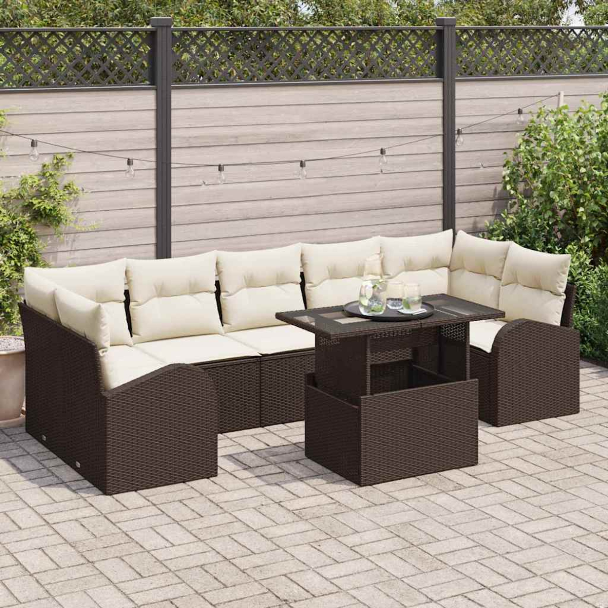 Garten-Sitzgruppe mit braunem Korbgeflecht, cremefarbenen Kissen und einem Tisch mit Hubfunktion. Auf einer Ziegelterrasse mit Zaun und Grün im Hintergrund.