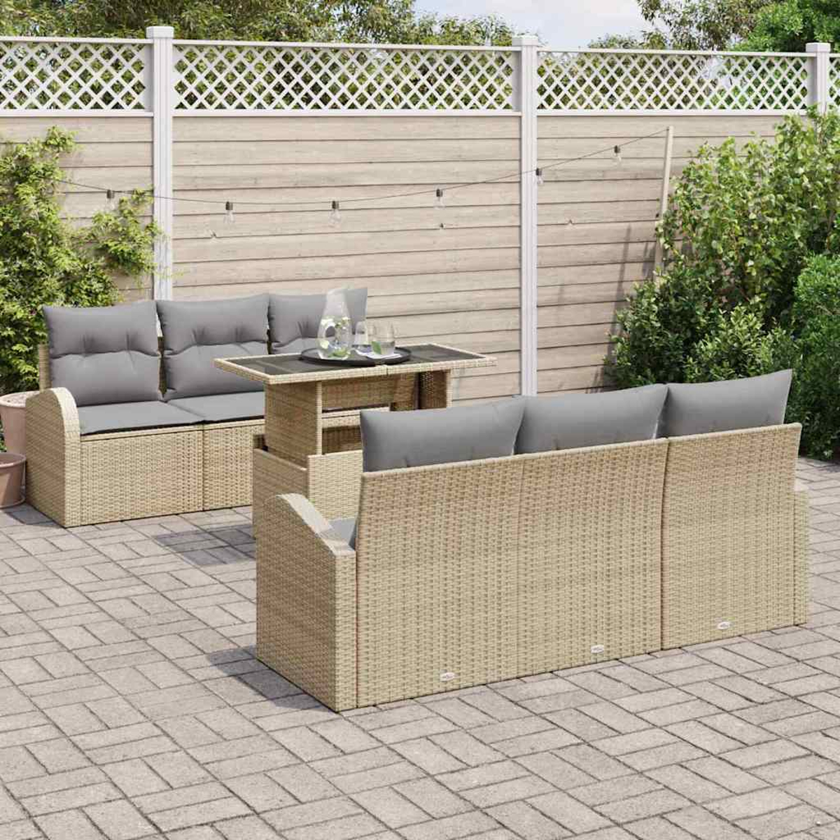 Terrassenmöbel-Set im Freien mit beigen Korbmöbeln, grauen Kissen und einem Tisch mit Glasplatte auf einer Ziegelterrasse, vor einem Zaun.