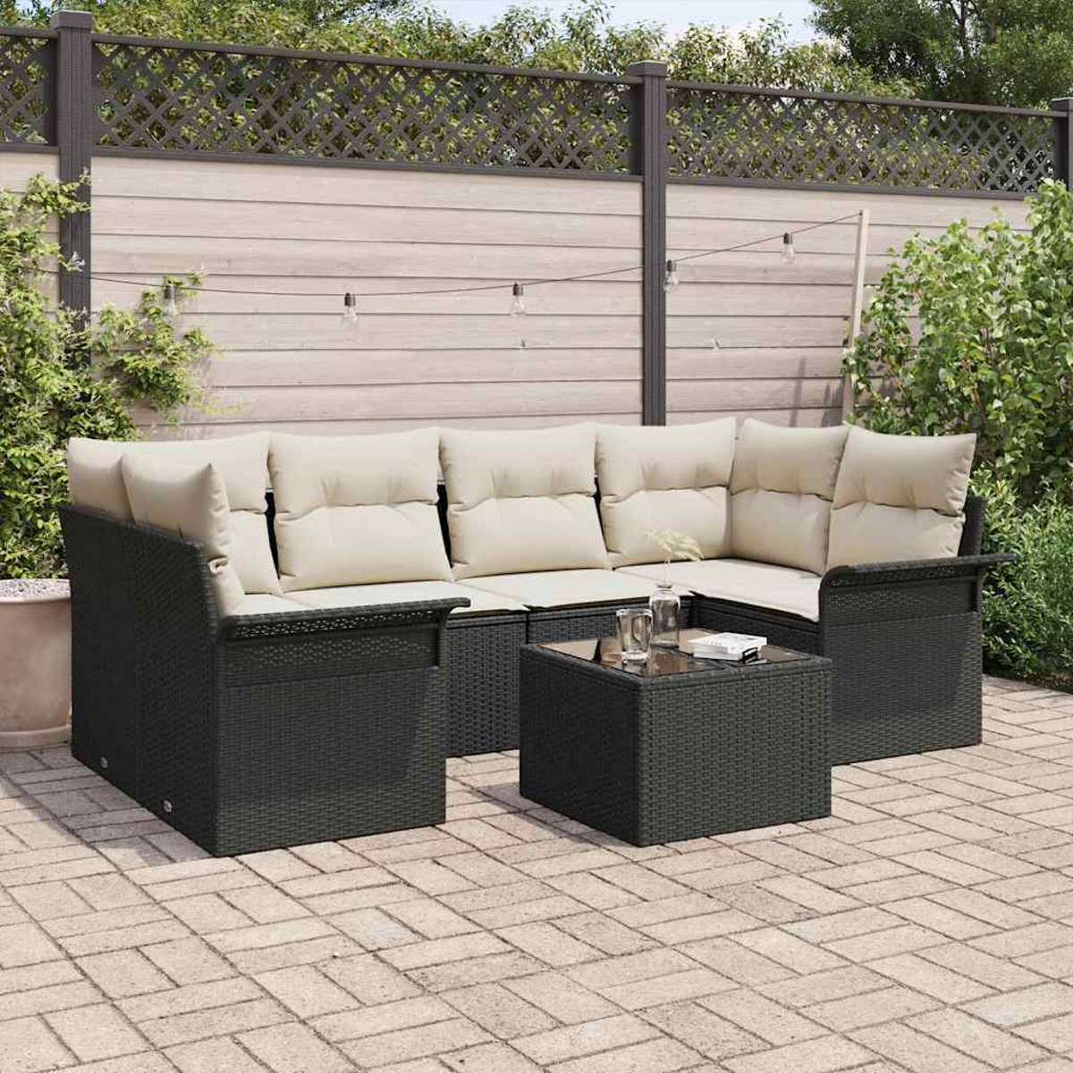 Sofá seccional para exteriores con cojines beige y una mesa pequeña. Ubicado en un patio de ladrillos, con una valla de madera y luces en el fondo.