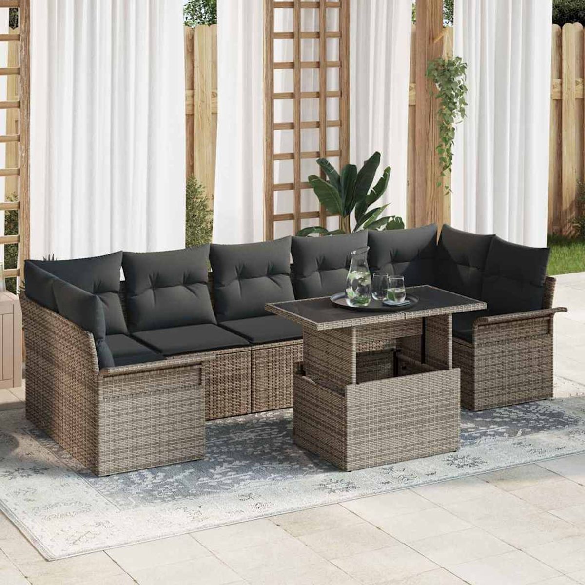 Gartenmöbel aus Korbgeflecht mit grauen Kissen. Ein kleiner Tisch mit einem Glas Wasser. Weiße Vorhänge und Holzgitter im Hintergrund.