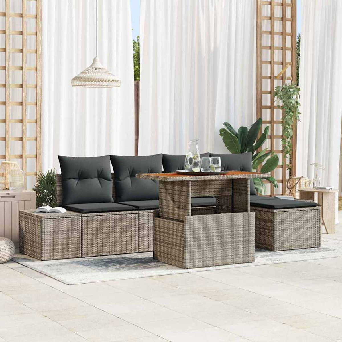 Outdoor-Sitzbereich mit Rattange Möbeln, grauen Kissen, einem Tisch und weißen Vorhängen im Hintergrund.