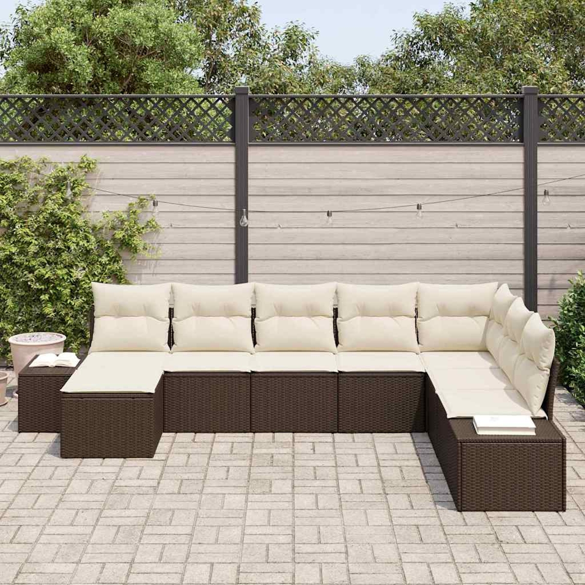 Ein Ecksofa mit cremefarbenen Kissen im Freien steht auf einer Terrasse. Ein Holzzaun und Bäume sind im Hintergrund.