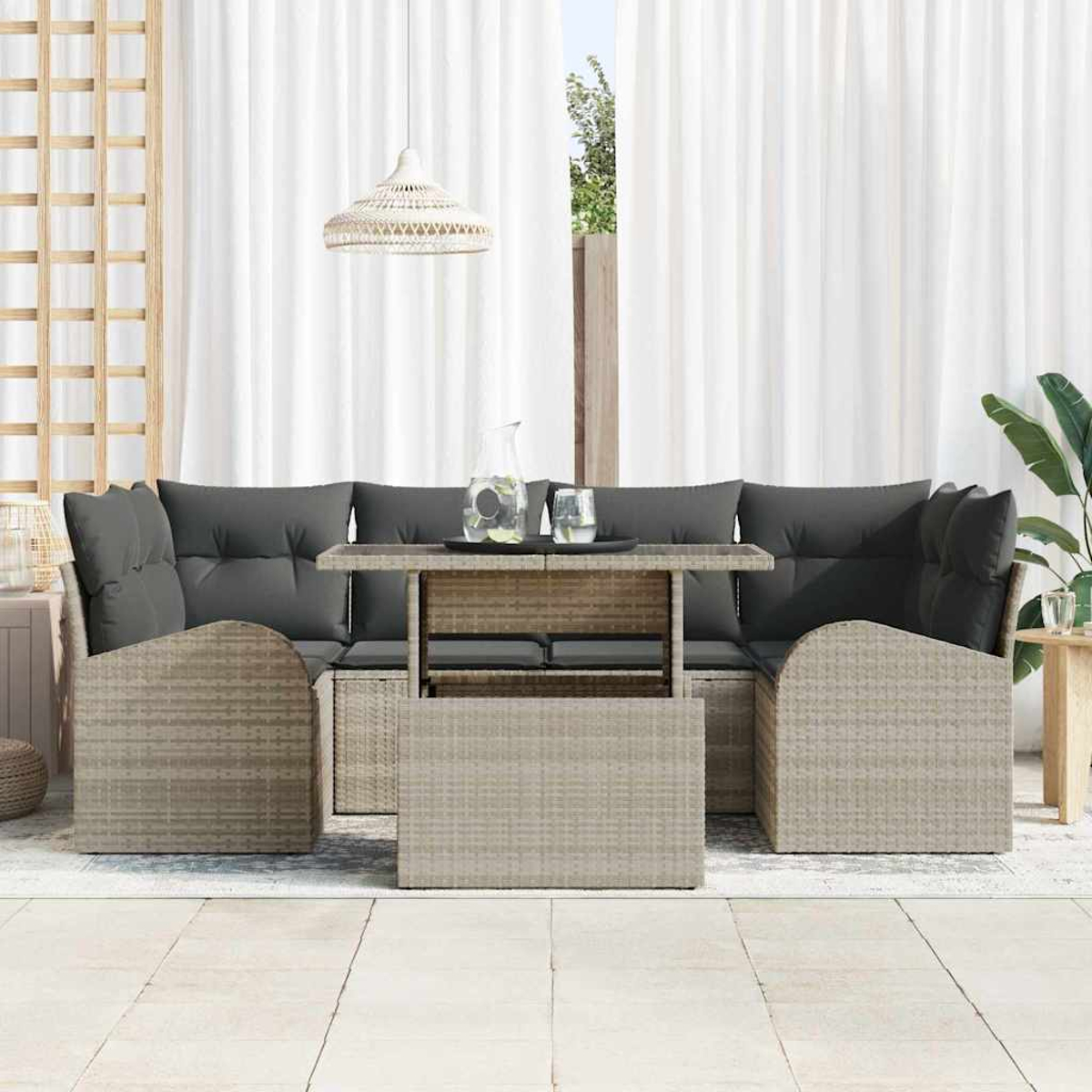 Outdoor-Korbsitzgruppe mit grauen Kissen und einem Tisch. Weiße Vorhänge und eine Pflanze im Hintergrund. Eine Lampe hängt darüber.