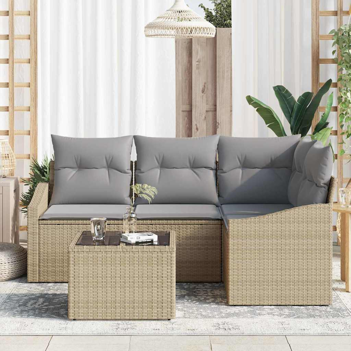 Rattansofa im Freien mit grauen Kissen und einem kleinen Tisch. Im Hintergrund ein weißer Vorhang und Pflanzen.
