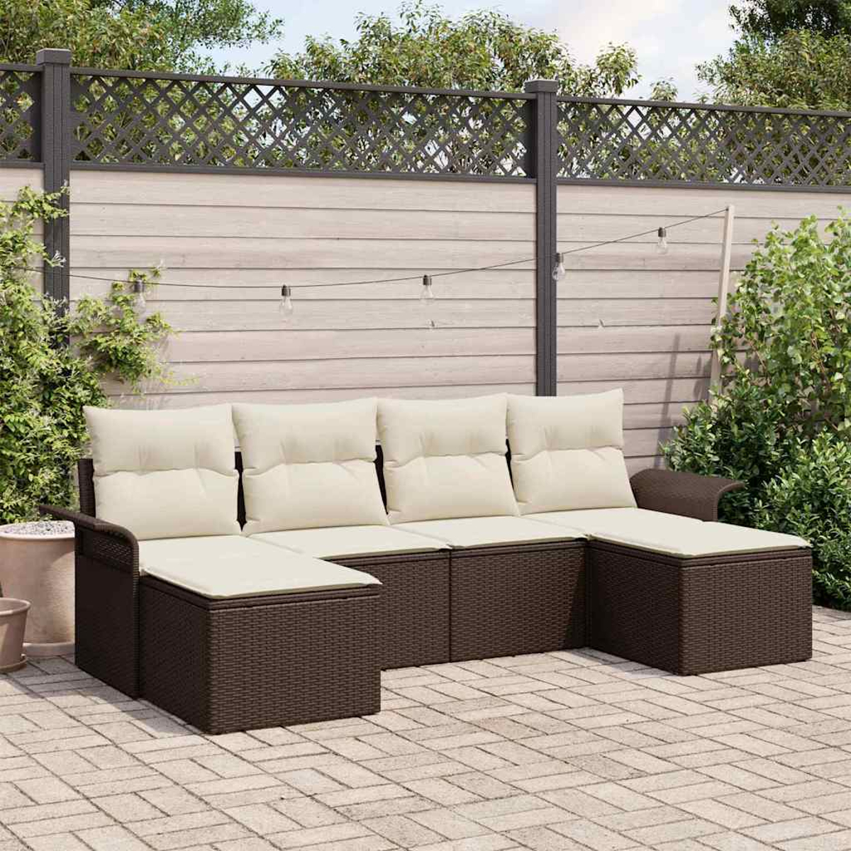 Ein braunes Outdoor-Sofa aus Korbgeflecht mit cremefarbenen Kissen steht auf einer Ziegelterrasse. Im Hintergrund sind ein Zaun und Pflanzen zu sehen.