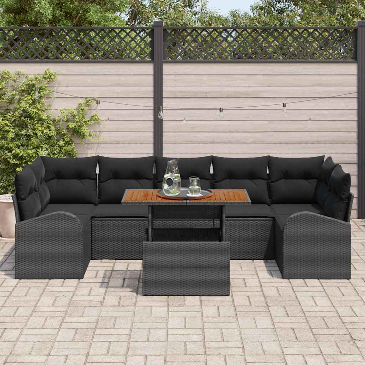 Garten-Terrassenset: schwarzes Korbmöbel-Ecksofa mit schwarzen Kissen, Holztisch und einem Glas Wasser. Hintergrund: Zaun.