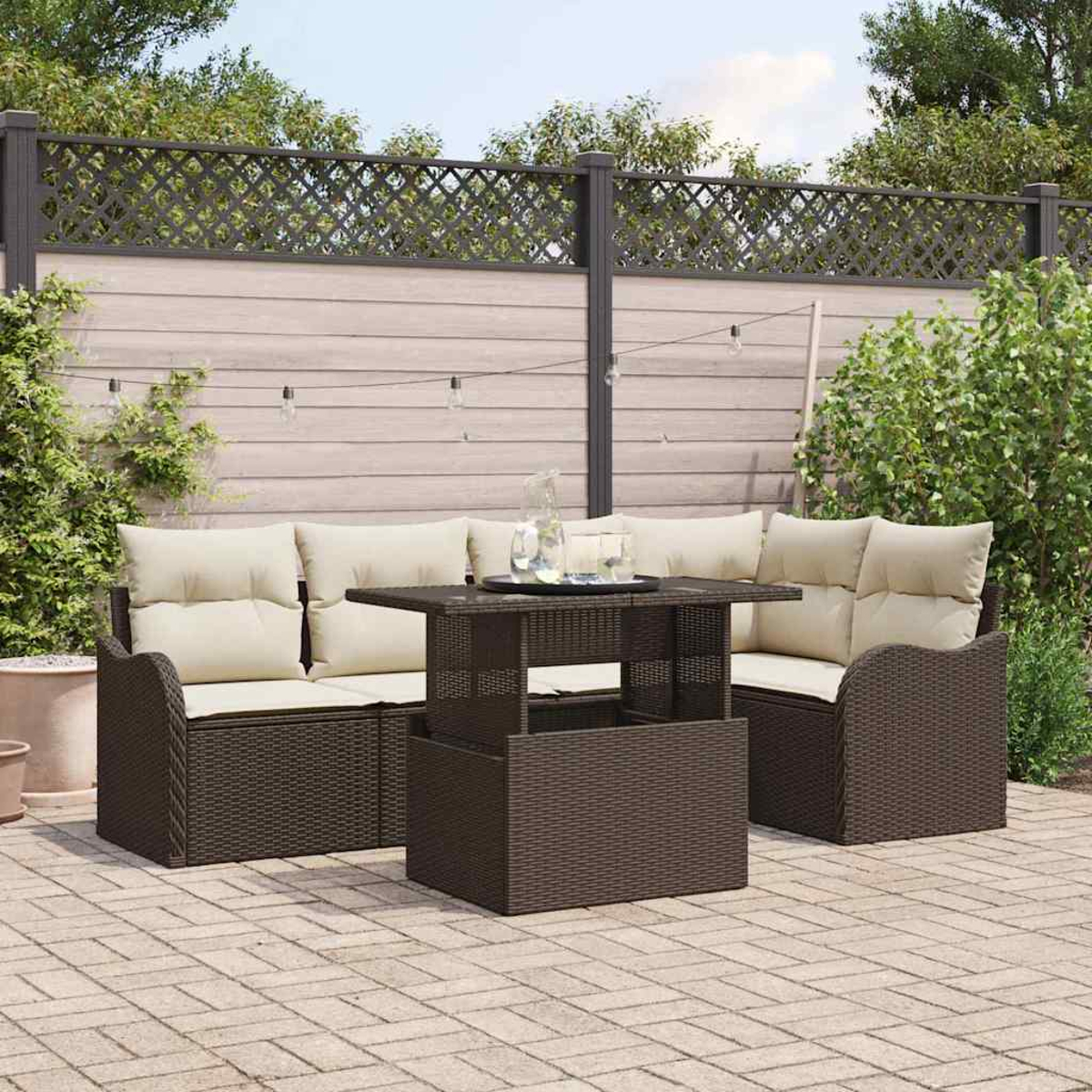 Outdoor-Terrassenset mit braunen Korbmöbeln, beigen Kissen und einem Tisch. Im Hintergrund befinden sich ein Zaun und Grün.