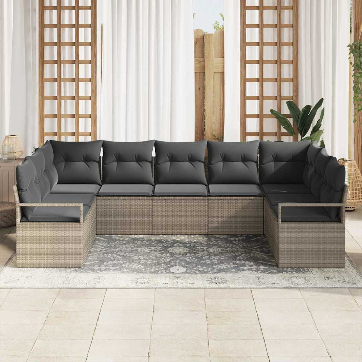 Ein großes, U-förmiges Outdoor-Sofa mit grauen Kissen steht auf einem gemusterten Teppich in der Nähe eines Fensters mit weißen Vorhängen.