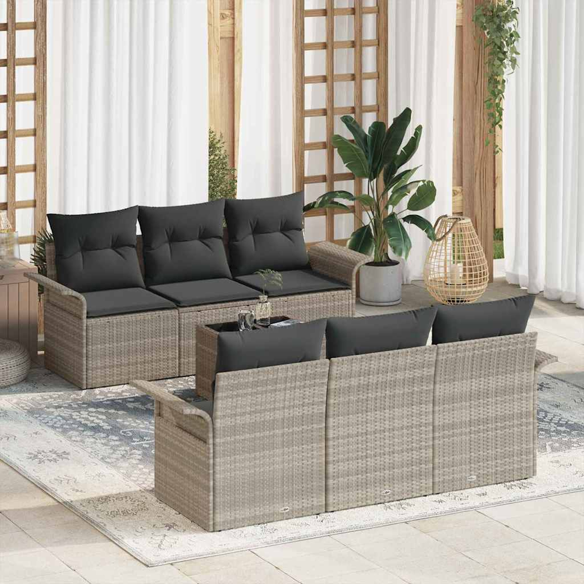 Garten-Terrassenset mit grauen Kissen, Korbmöbeln und einem Teppich. Eine große Pflanze und eine Laterne befinden sich im Hintergrund. Weiße Vorhänge sind sichtbar.