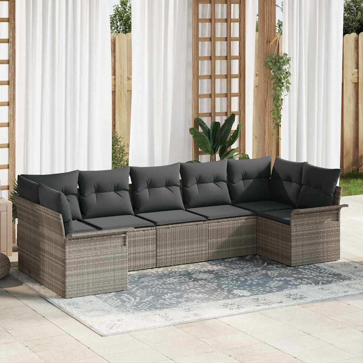 Ein graues Korbsessel-Sofa mit dunkelgrauen Kissen steht auf einem Teppich. Weiße Vorhänge und Holzrahmen befinden sich im Hintergrund.