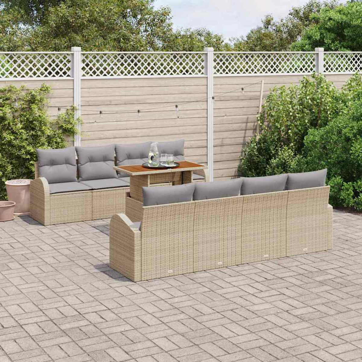 Garten-Sitzgruppe auf einer Terrasse. Beige Korbsessel mit grauen Kissen und einem kleinen Tisch. Ein weißer Zaun und grüne Pflanzen im Hintergrund.