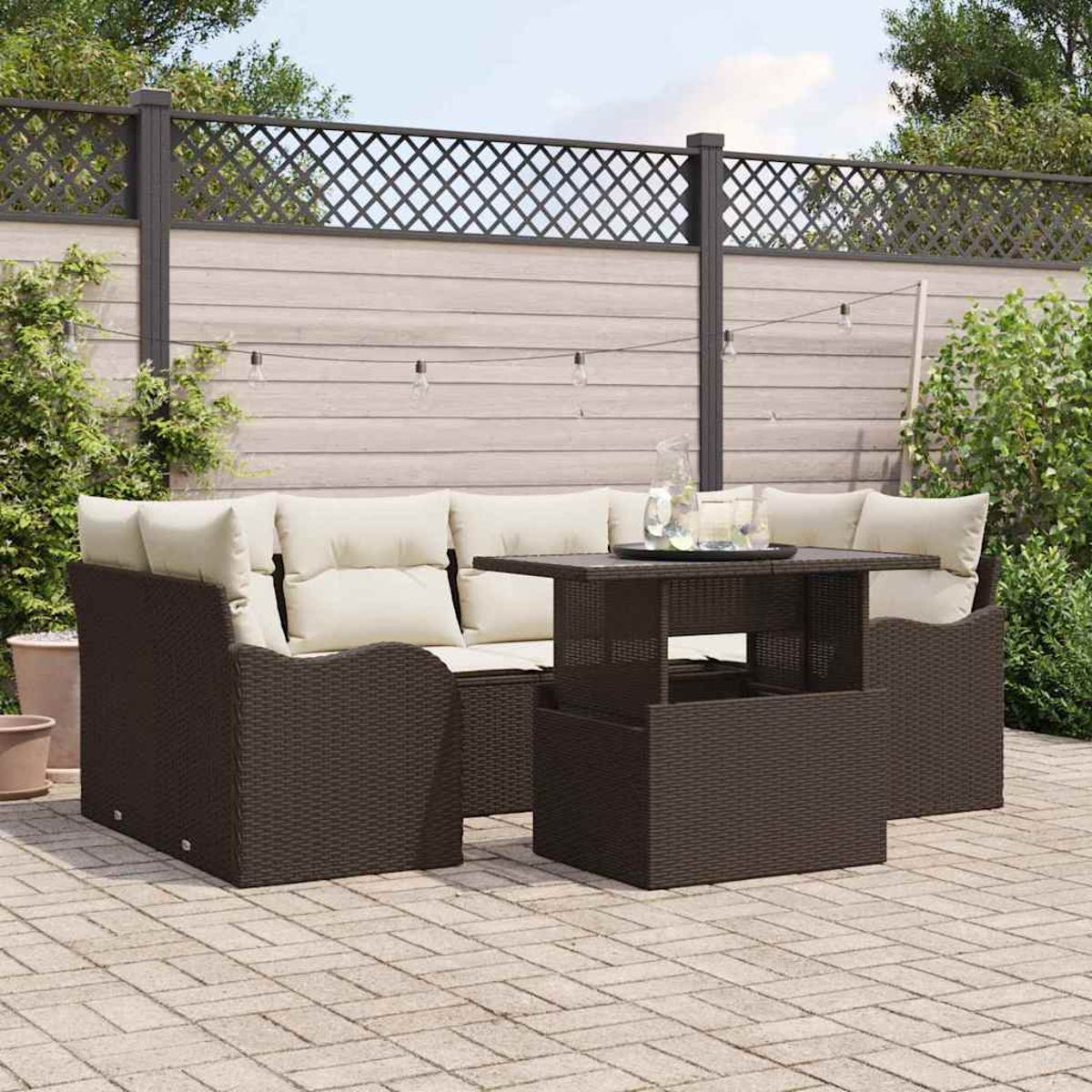 Garten-Terrassenset mit braunen Korbmöbeln, weißen Kissen und einem Tisch. Hintergrund ist ein Zaun und Grün.