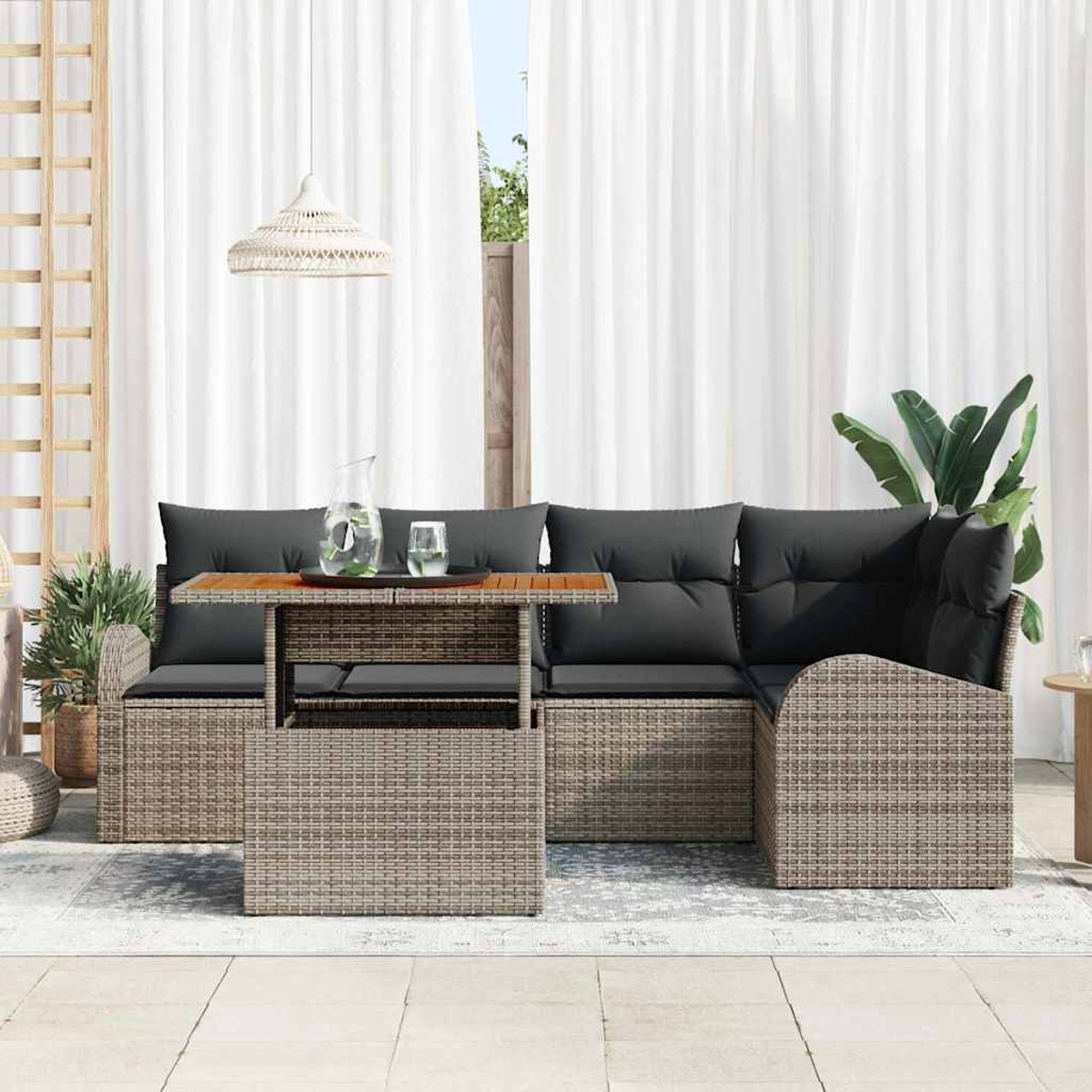 Gartenmöbel-Set aus Korbgeflecht mit Tisch, Sofa mit schwarzen Kissen, weißen Vorhängen und einer Hängelampe. Auch Pflanzen sind sichtbar.