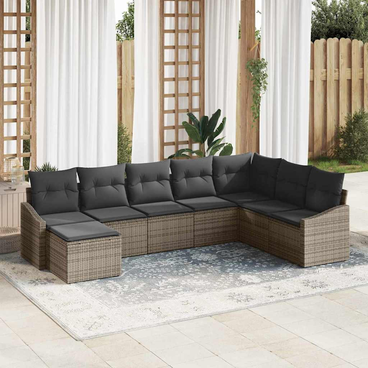 Ein Outdoor-Ecksofa mit grauen Kissen steht auf einem gemusterten Teppich. Weiße Vorhänge und ein Holzzaun sind im Hintergrund.