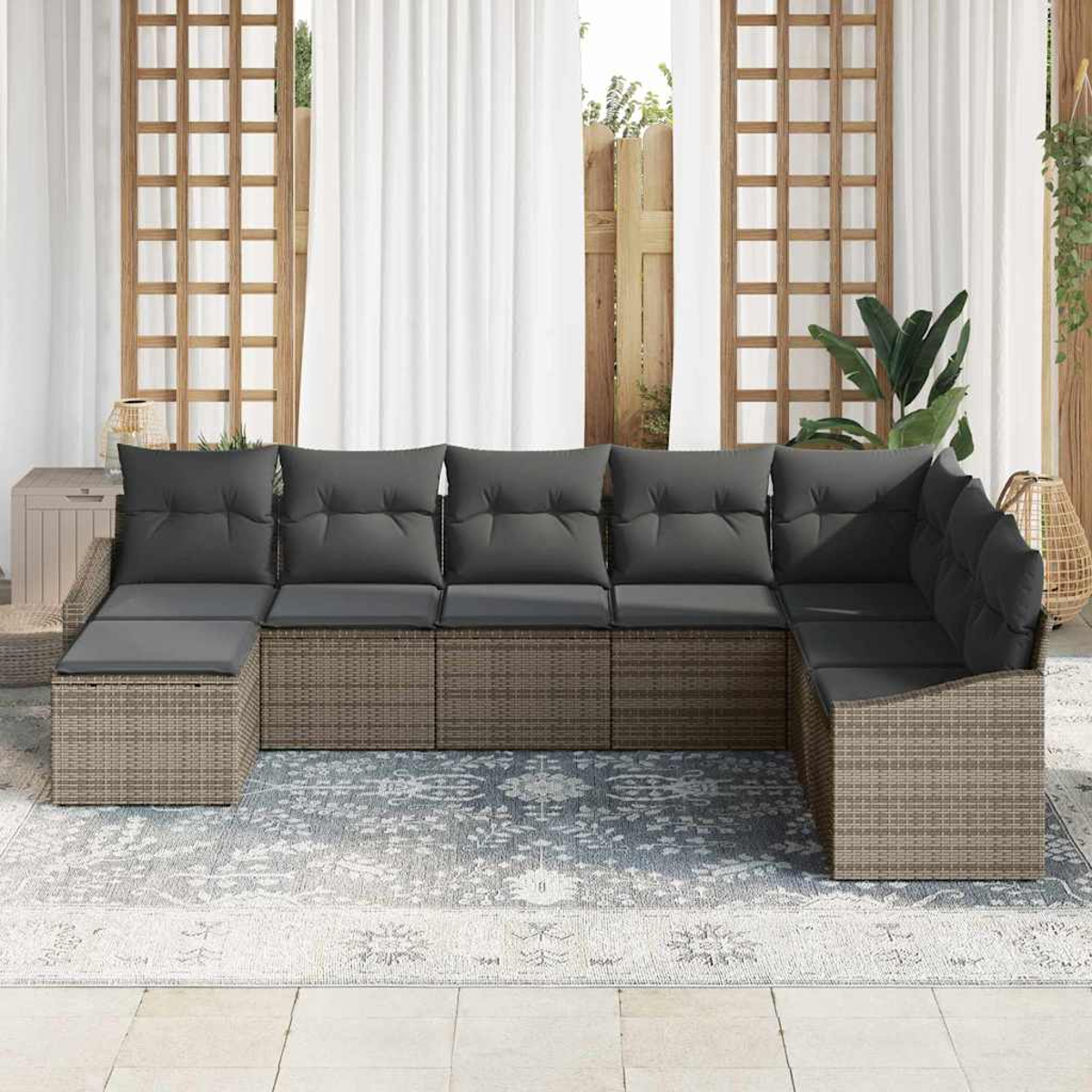 Outdoor-Ecksofa mit grauen Kissen auf einem gemusterten Teppich. Hintergrund: weiße Vorhänge, Holzgitter und Pflanzen.