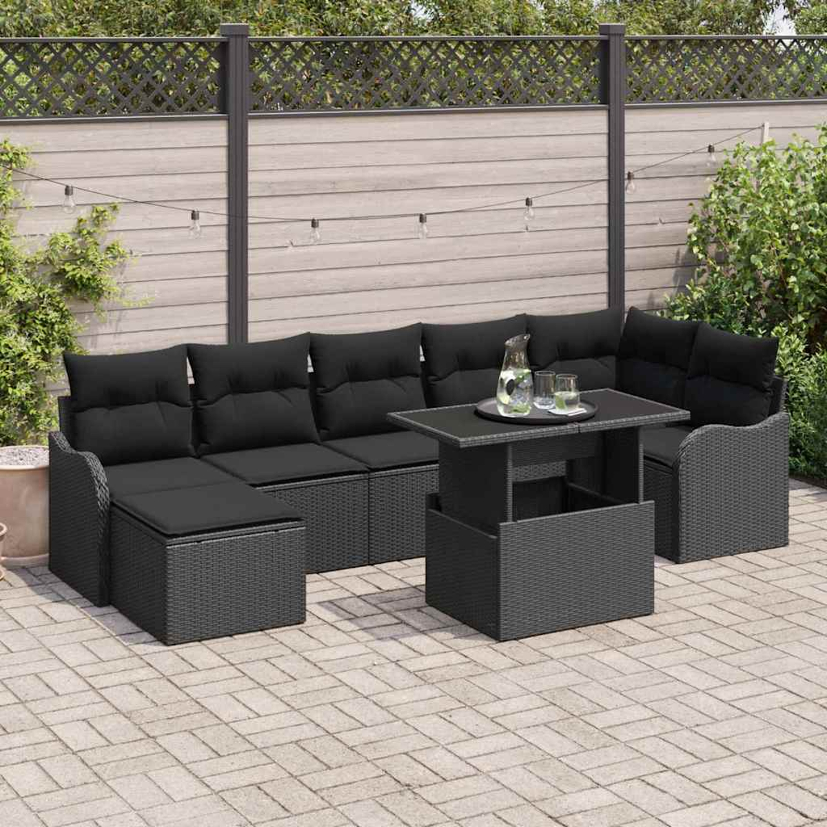 Gartenmöbel mit schwarzen Kissen und einem grauen Tisch. Auf dem Tisch stehen eine Wasserkaraffe und Gläser. Die Umgebung ist eine Terrasse.