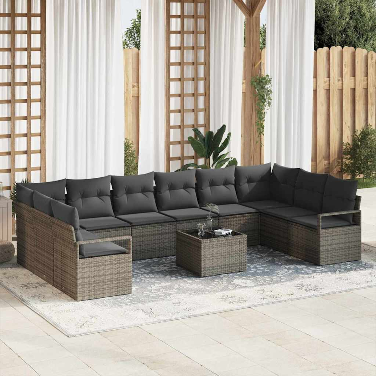 Outdoor-Terrassenset mit grauen Kissen, einem Couchtisch und weißen Vorhängen im Hintergrund. Das Set steht auf einem gemusterten Teppich.