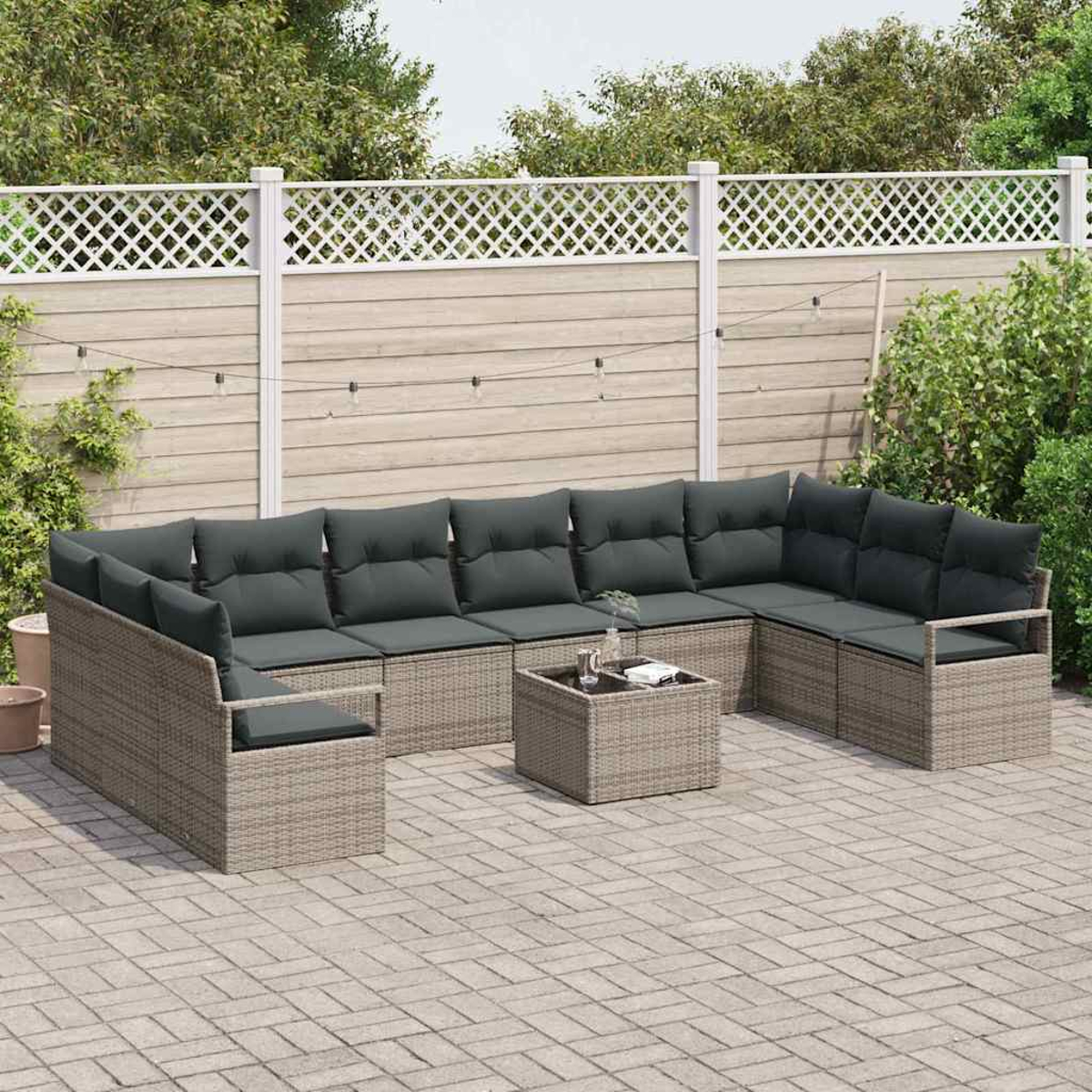 Garten-Sitzgruppe mit grauen Kissen und einem Couchtisch auf einer gepflasterten Terrasse. Ein weißer Gitterzaun und grüne Sträucher sind im Hintergrund.
