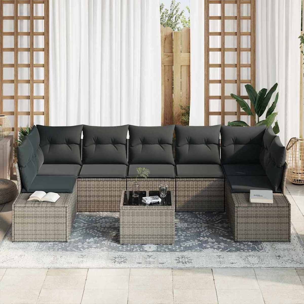 Outdoor-Ecksofa mit grauen Kissen, einem kleinen Tisch und einem gemusterten Teppich. Dahinter befinden sich Holzgitter und weiße Vorhänge.