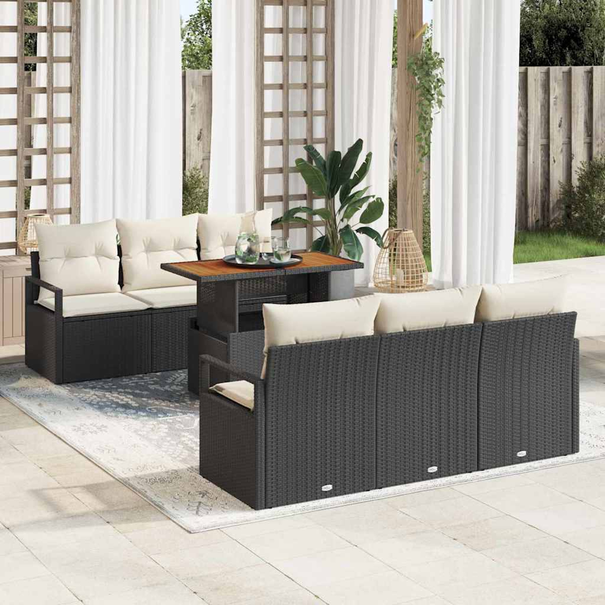 Terrassenmöbel-Set mit schwarzem Korbmöbeln, cremefarbenen Kissen und einem Holztisch. Weiße Vorhänge und Pflanzen im Hintergrund.