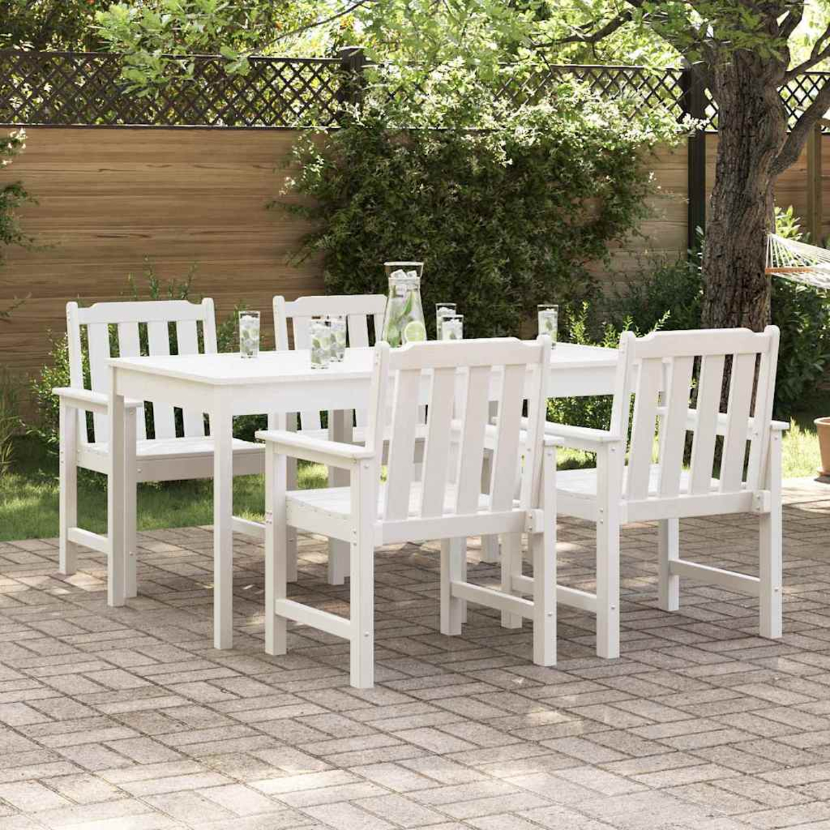 Weißes Esszimmer-Set für den Außenbereich mit Tisch und Stühlen auf einer Terrasse. Gläser und eine Kanne stehen auf dem Tisch. Der Hintergrund zeigt Bäume und einen Zaun.