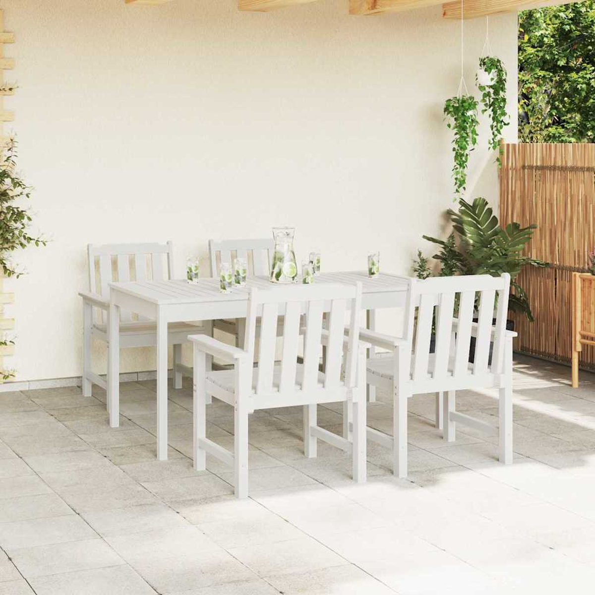 Ein weißes Holz-Terrassenset mit Tisch und Stühlen ist im Freien aufgebaut. Pflanzen und ein Bambuszaun sind im Hintergrund.