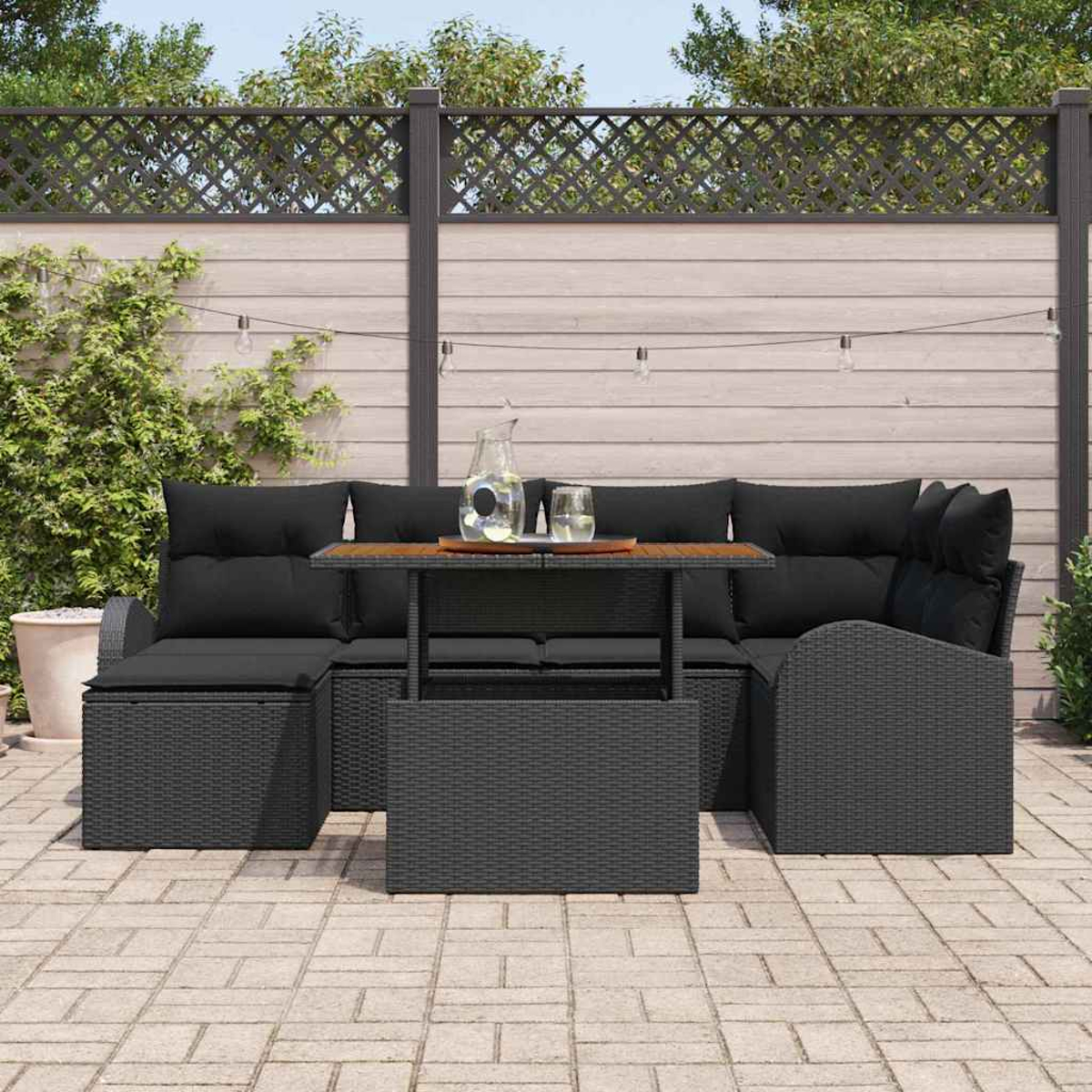 Garten-Sitzgruppe mit schwarzen Kissen, einem Holztisch und einem dekorativen Zaun. Inklusive Wasserkrug und Gläsern.