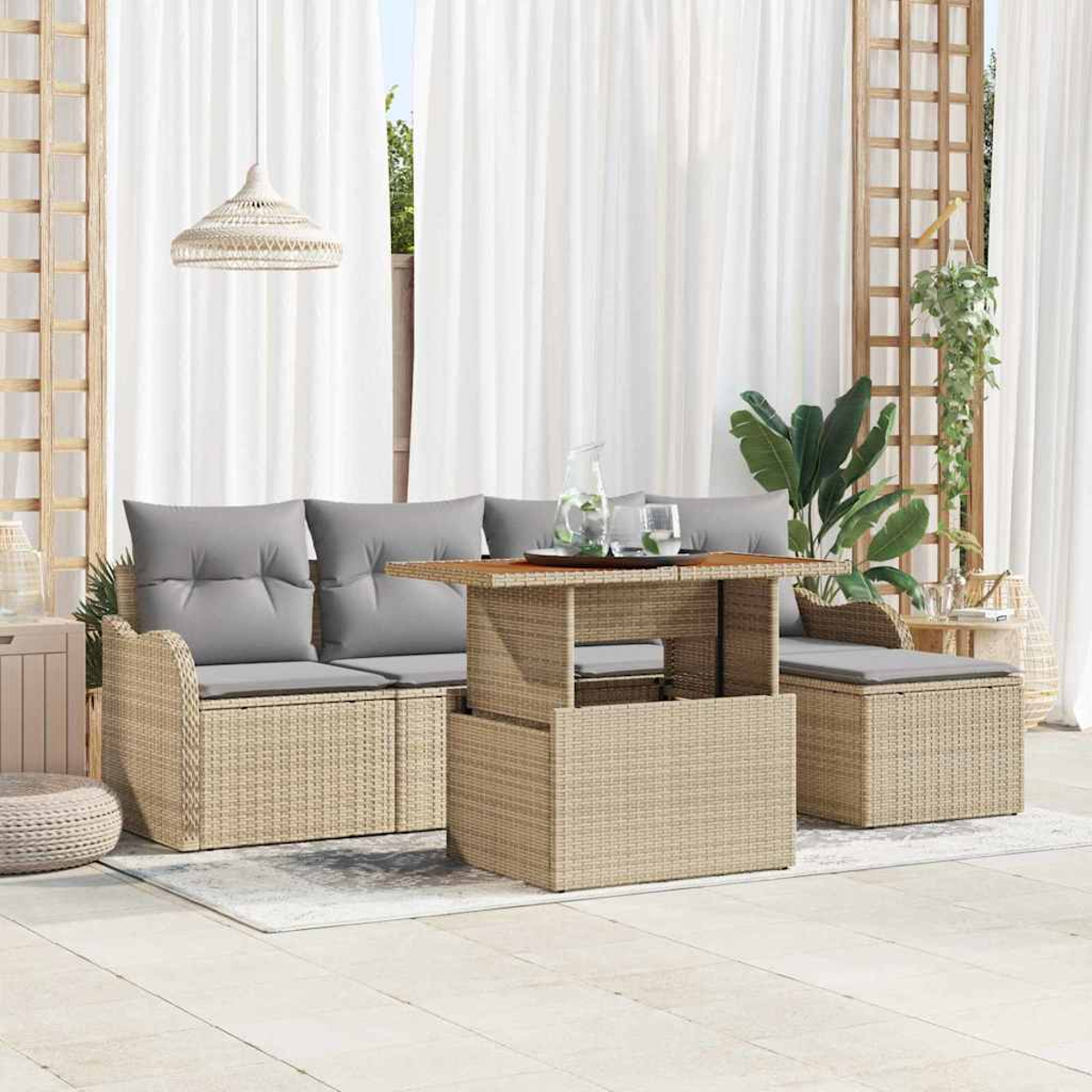 Gartenmöbel-Set aus Rattan: Sofa mit grauen Kissen, Tisch und Beistellstuhl. Weiße Vorhänge und Pflanzen im Hintergrund.