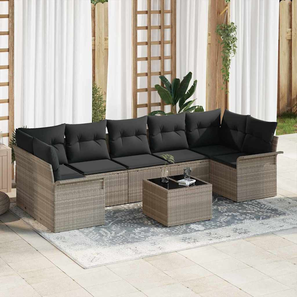 Gartenmöbel mit grauen Kissen und kleinem Tisch auf gemustertem Teppich. Dahinter weiße Vorhänge und Holzstruktur.