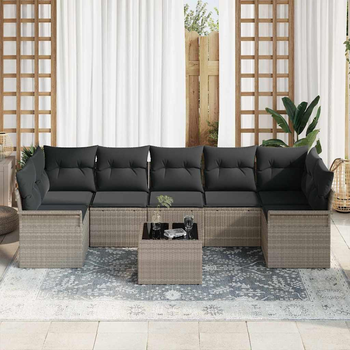 Outdoor-Ecksofa mit schwarzen Kissen auf einem gemusterten Teppich. Ein kleiner Tisch hat Gläser. Der Hintergrund umfasst weiße Vorhänge und Holzgitter.