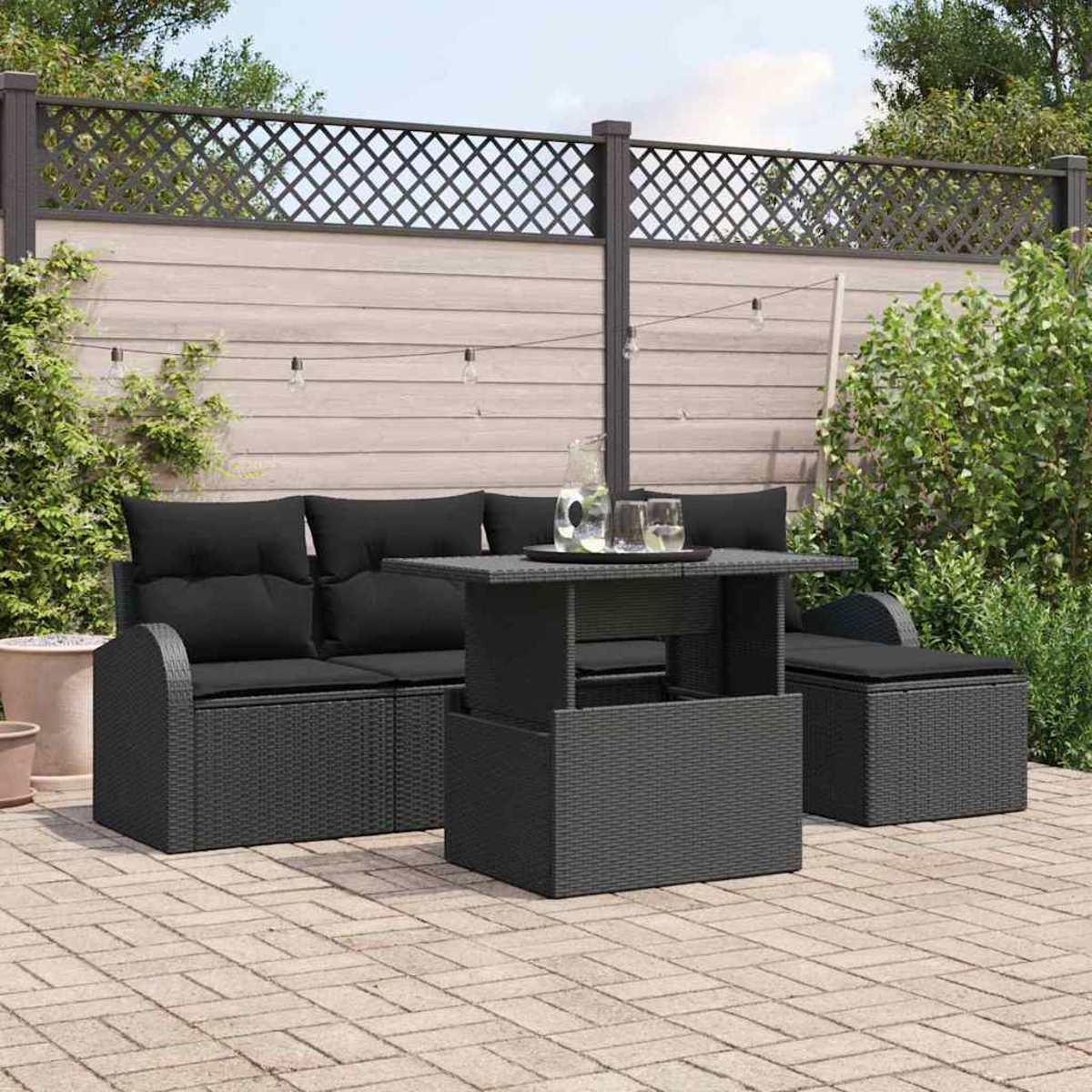Gartenmöbel-Set mit schwarzem Korbmöbel, Tisch und Ottomane. Im Hintergrund ein Zaun und Grün.